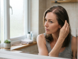 Une femme de 35 ans examine l'élargissement de sa raie au milieu dans un miroir de salle de bain pour augmenter la densité de ses cheveux.